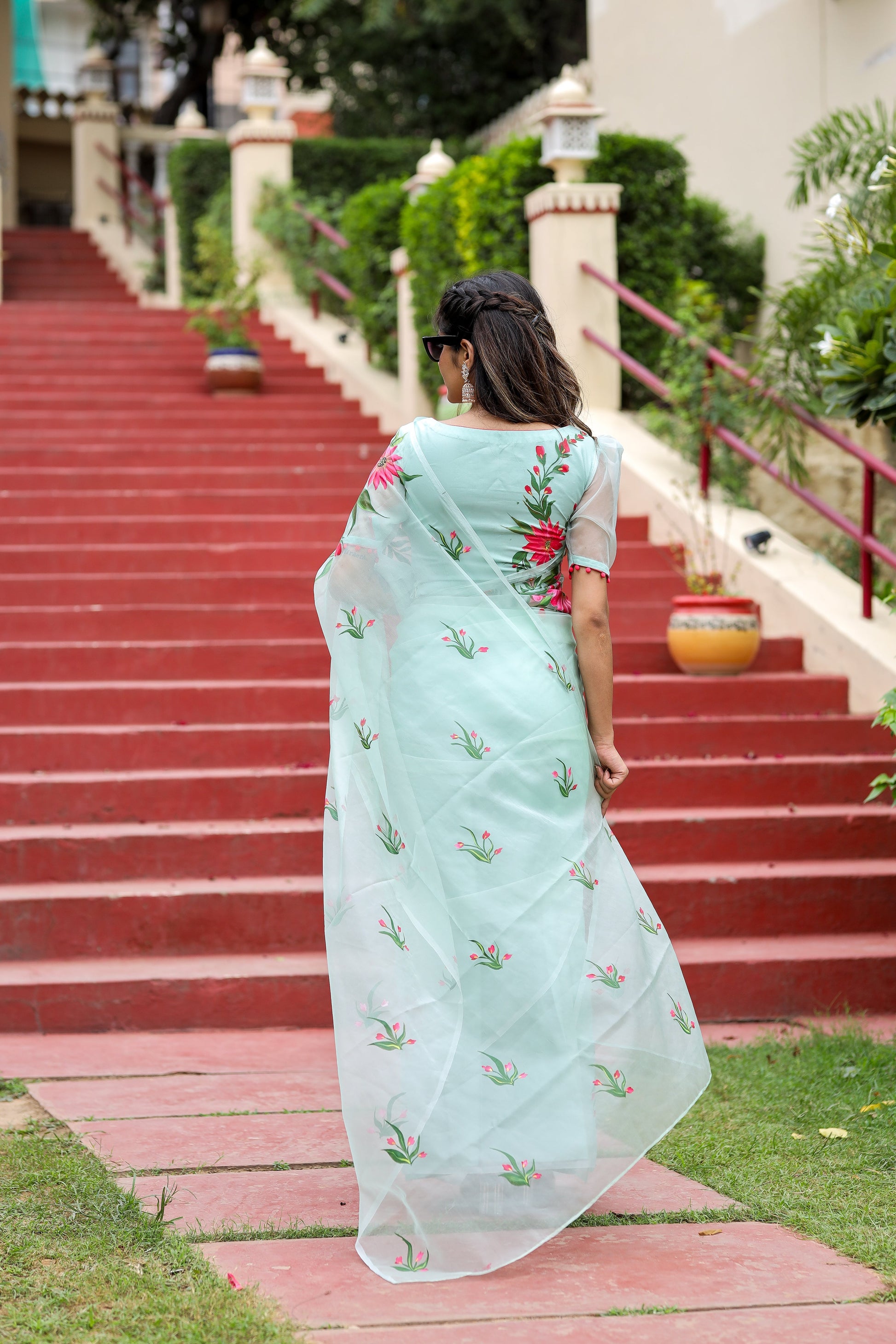 Elegant woman in a unique designer organza saree with floral embroidery walking down steps