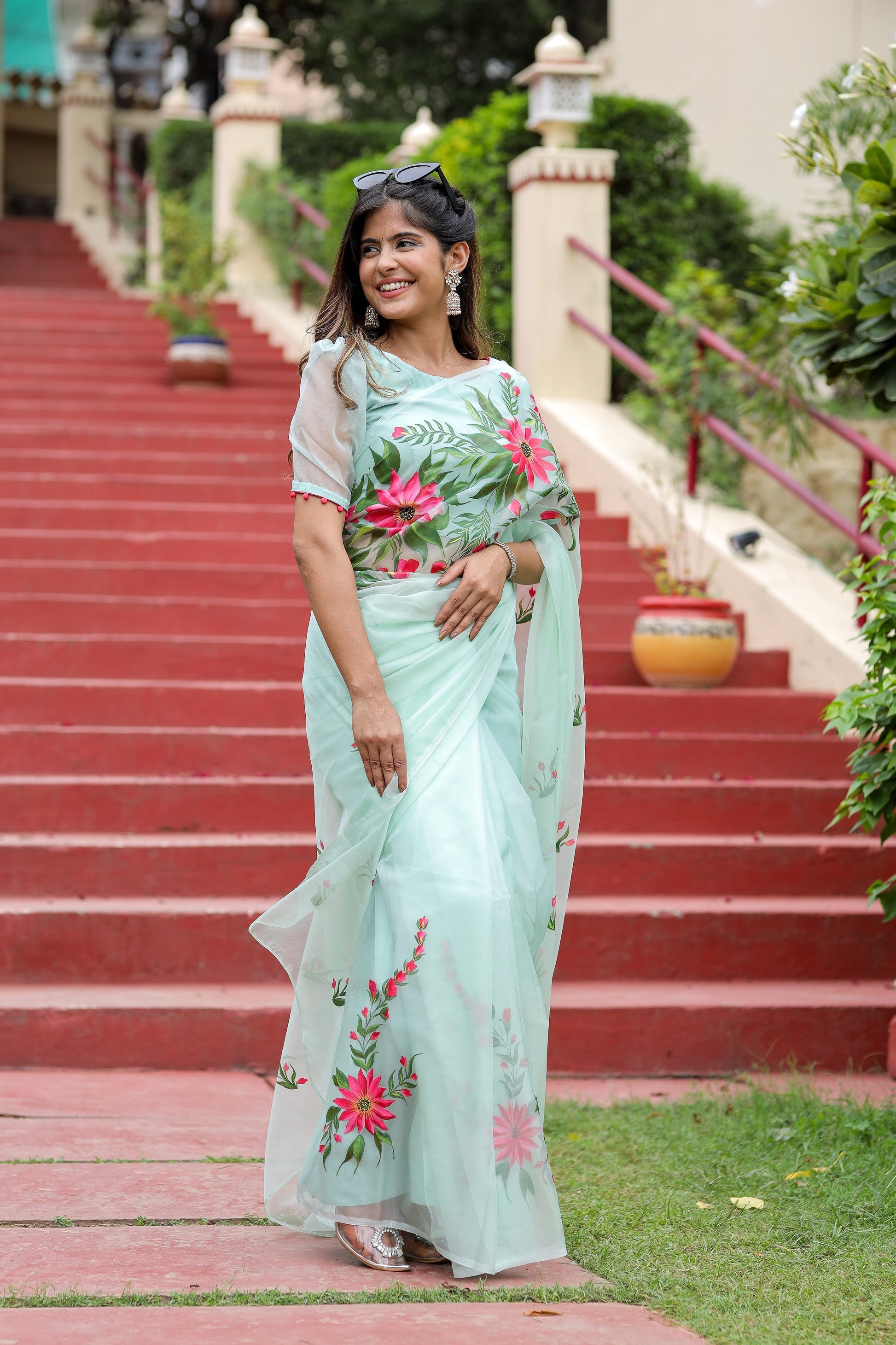 Elegant woman wearing a unique designer organza saree with floral embroidery on a sunny staircase