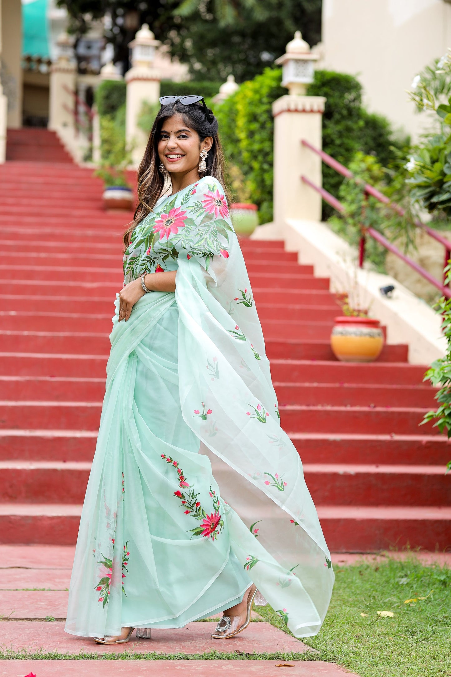 Beautiful woman modeling a unique designer organza saree with floral embroidery on a garden staircase