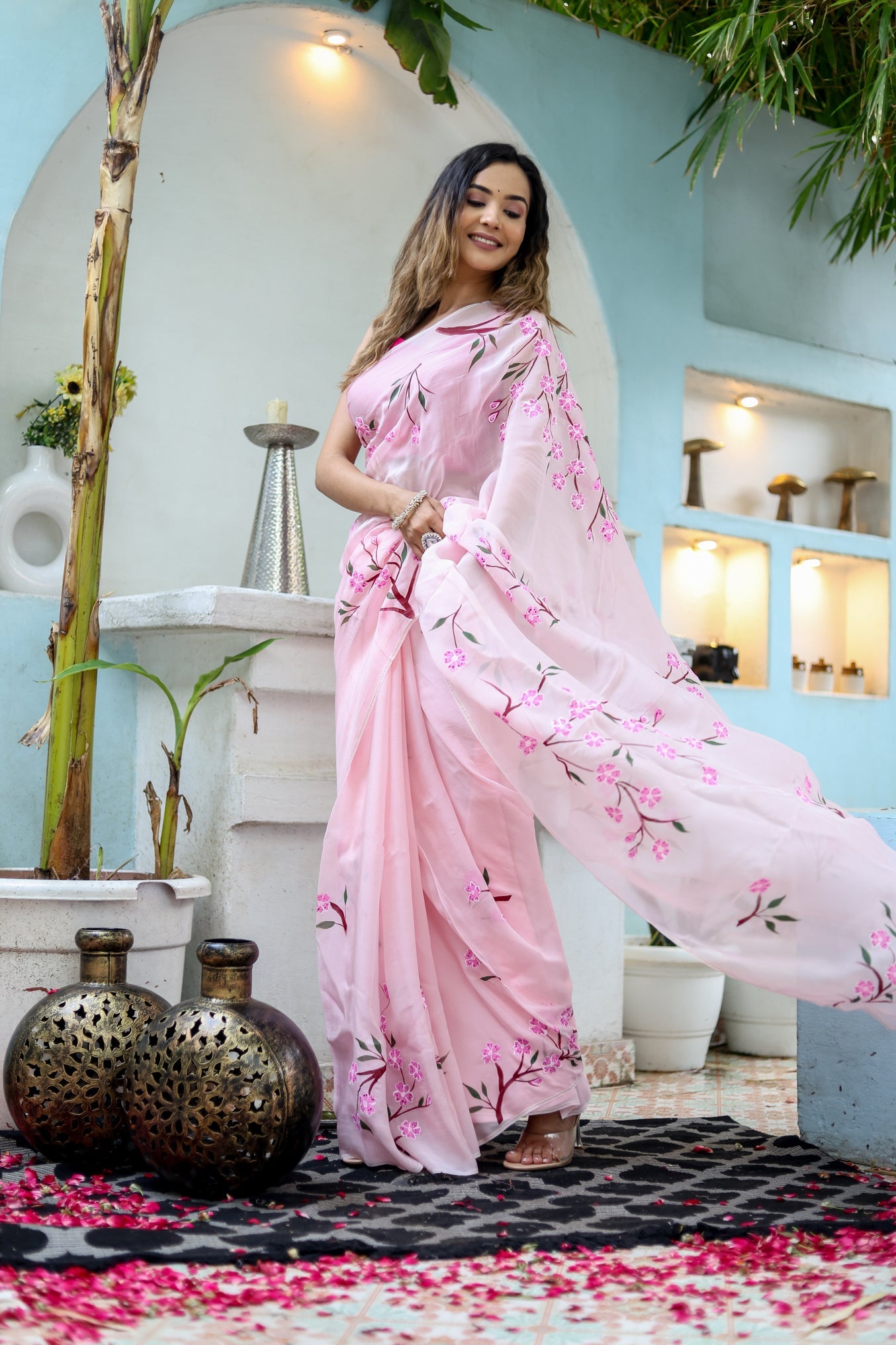 Elegant unique handpainted saree for weddings in soft pink with floral designs, worn by a model outdoors