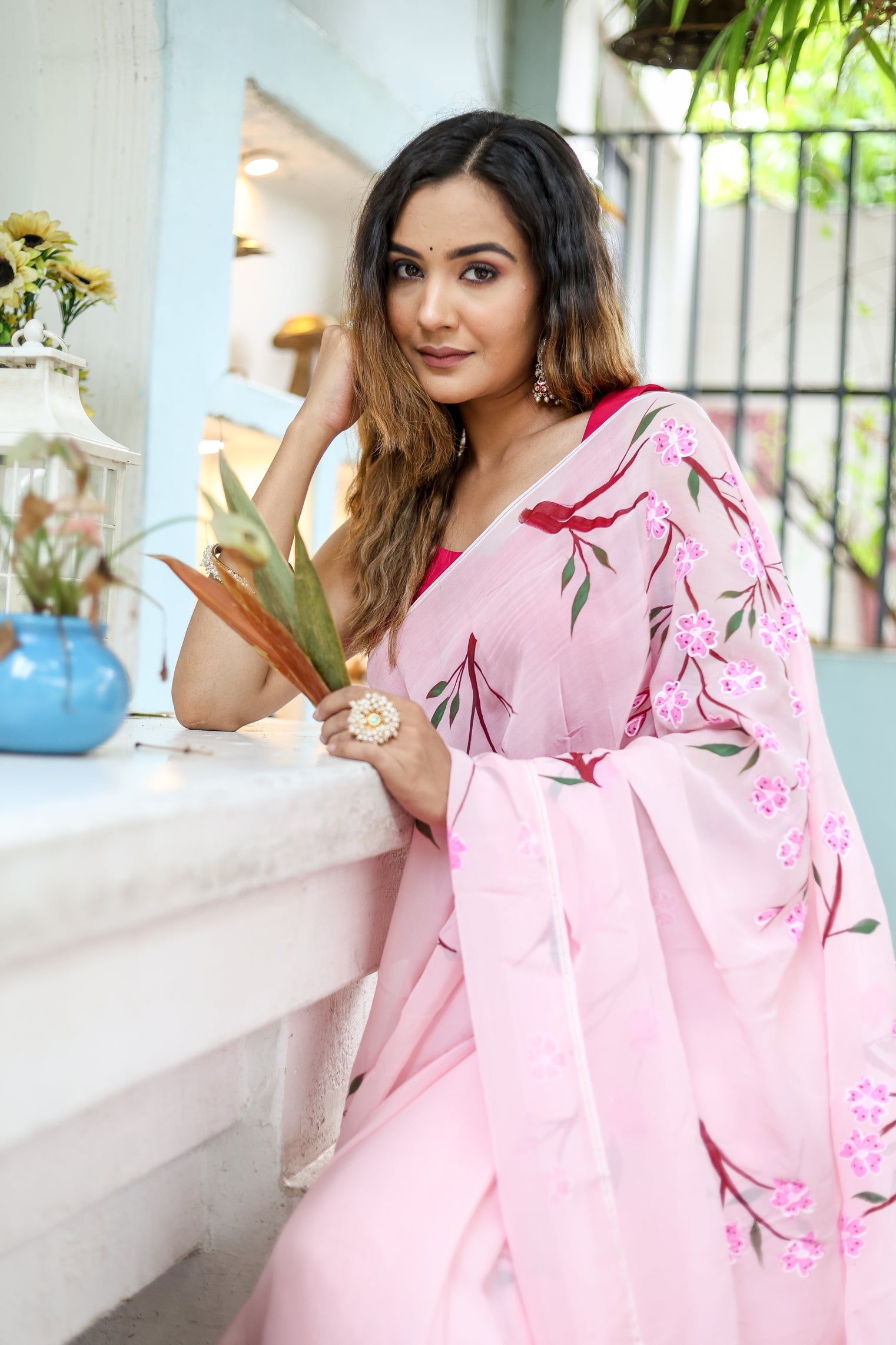 Elegant woman wearing a unique handpainted saree for weddings with floral designs, posing by a window