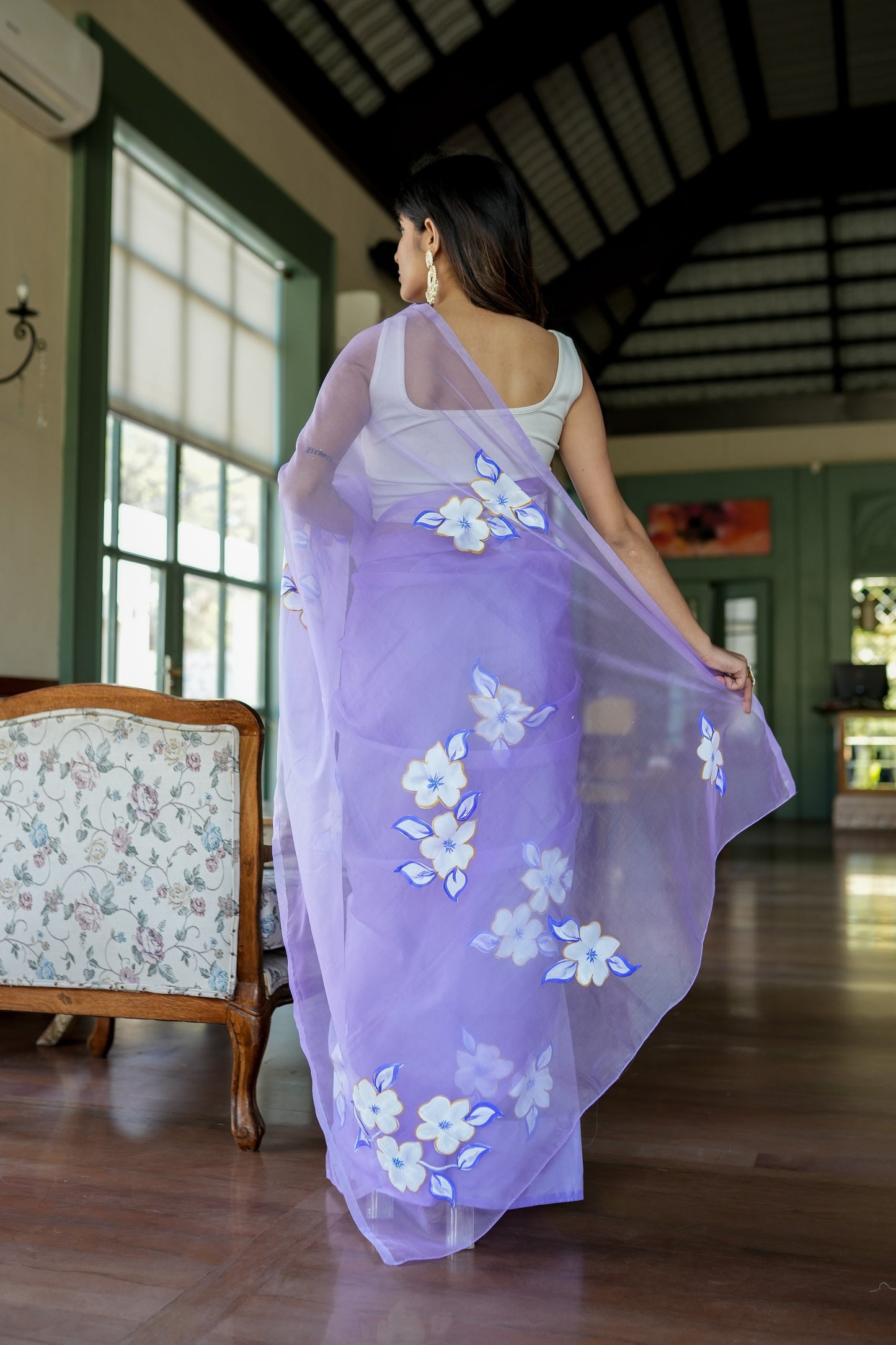 Model wearing a unique organza saree with artwork featuring floral designs in a serene indoor setting
