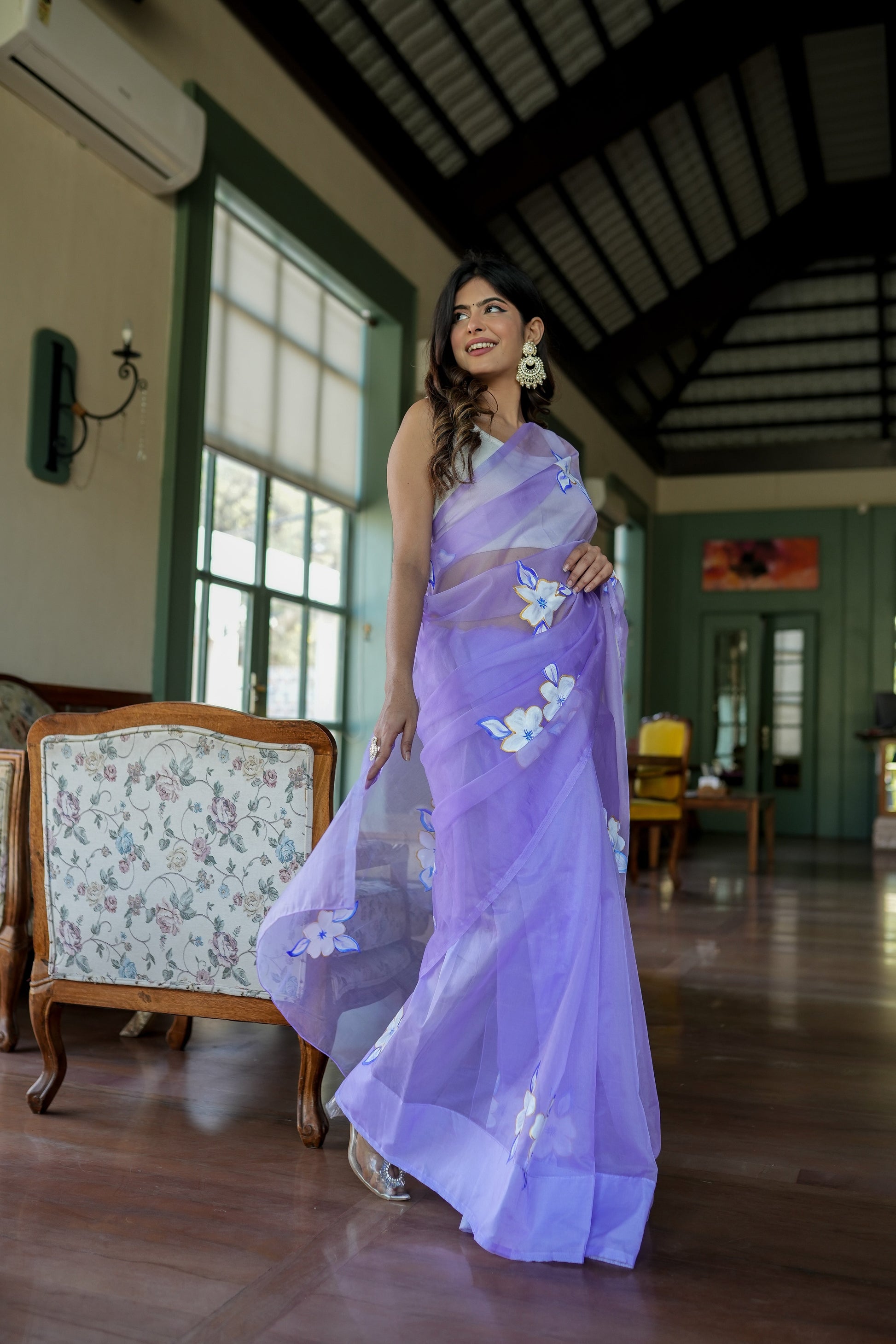 Elegant woman in a unique organza saree with artwork, standing indoors with floral designs