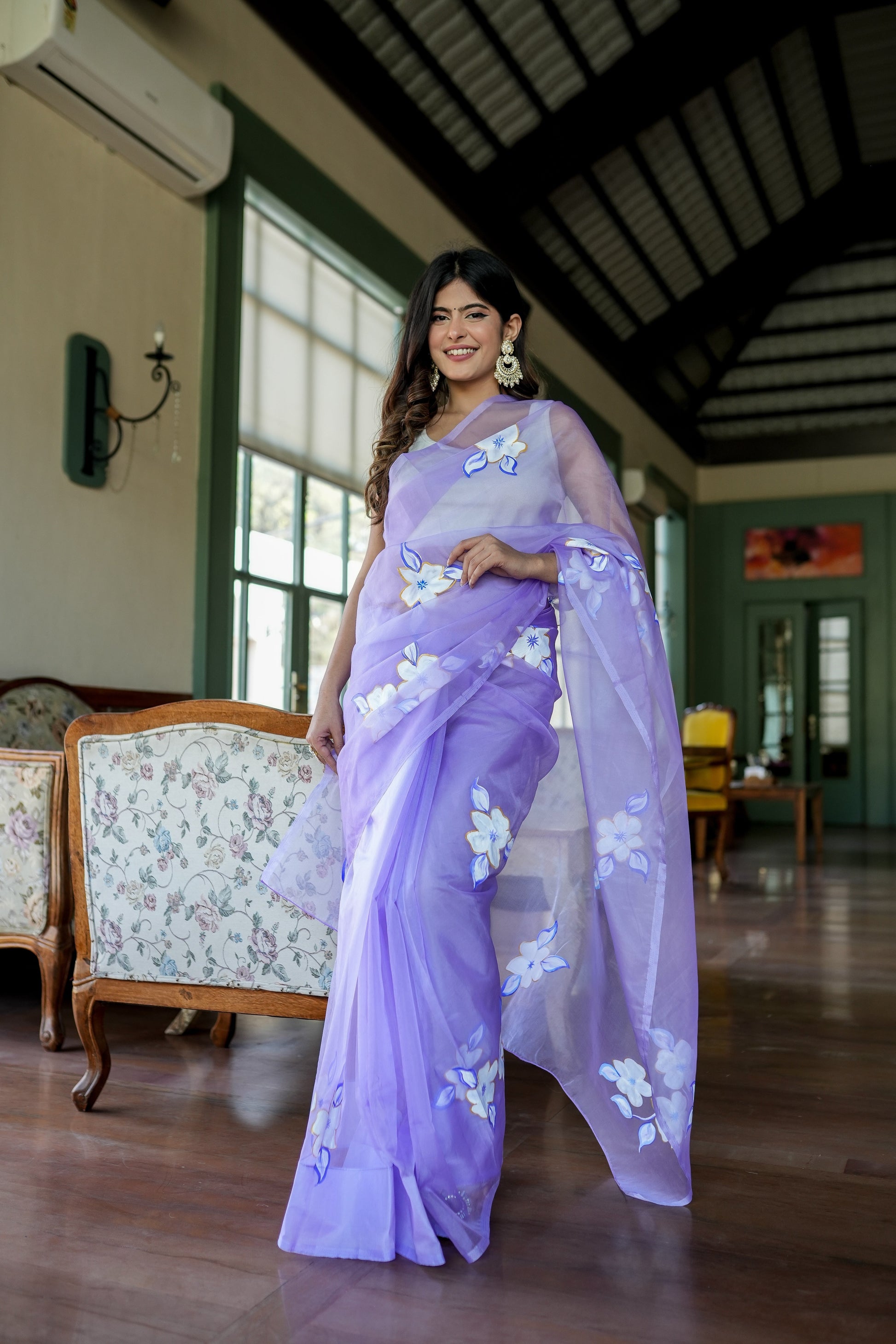 Woman wearing a unique organza saree with artwork in lavender color, showcasing elegant floral designs