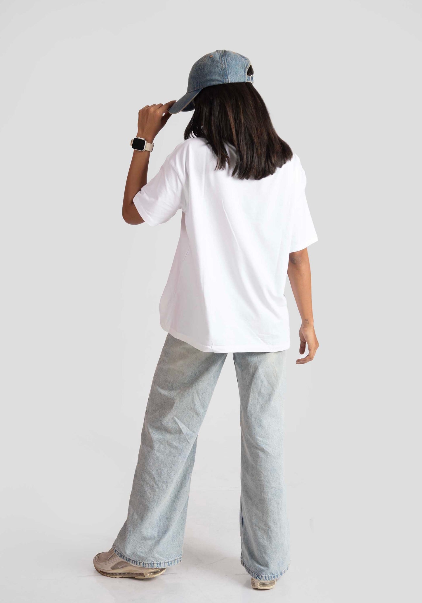 Back view of woman wearing white oversized anime t-shirt for women styled with wide-leg jeans and denim cap