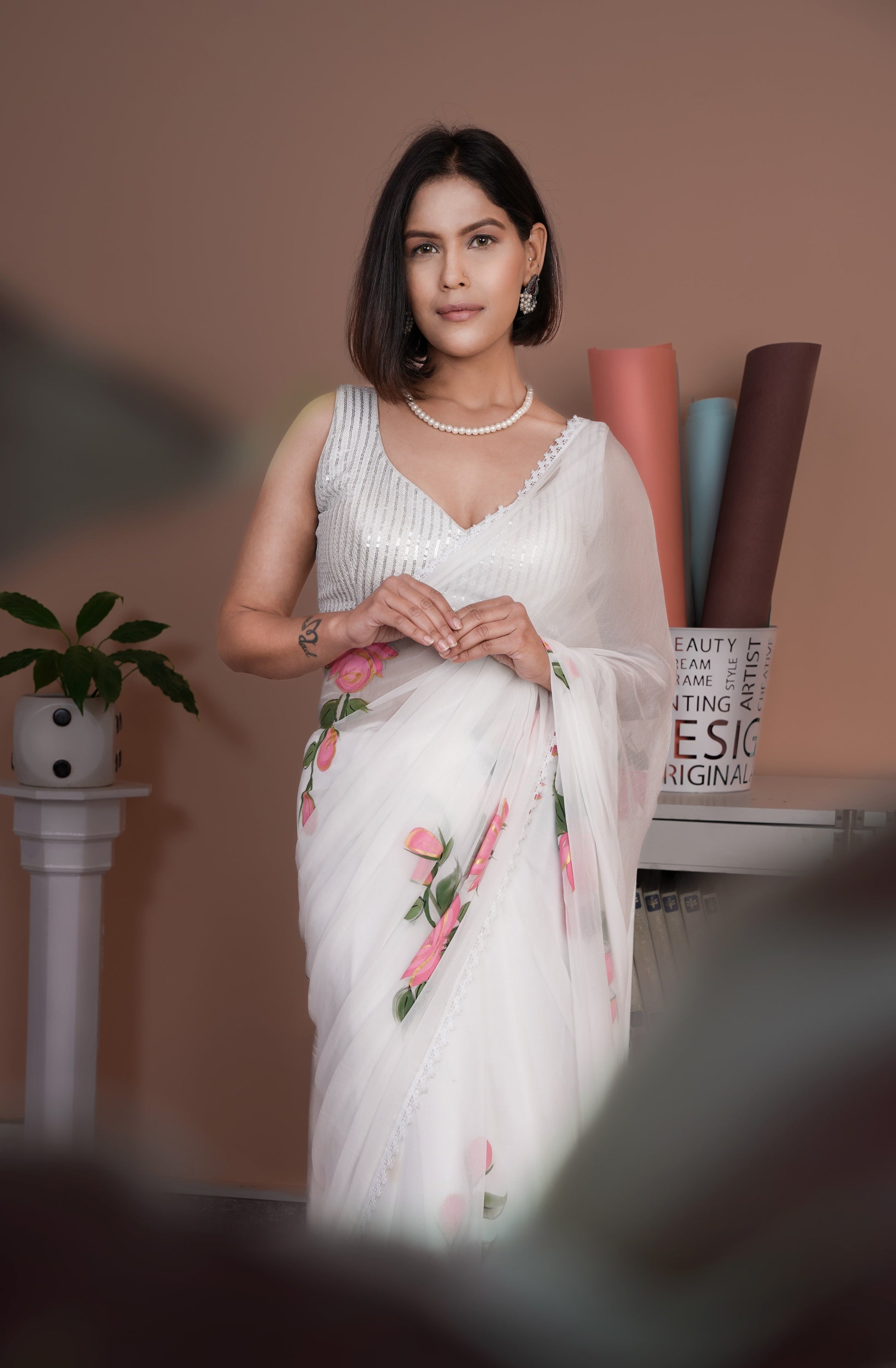 Elegant woman wearing a white saree with pink floral print, showcasing a sophisticated style with a lightweight design