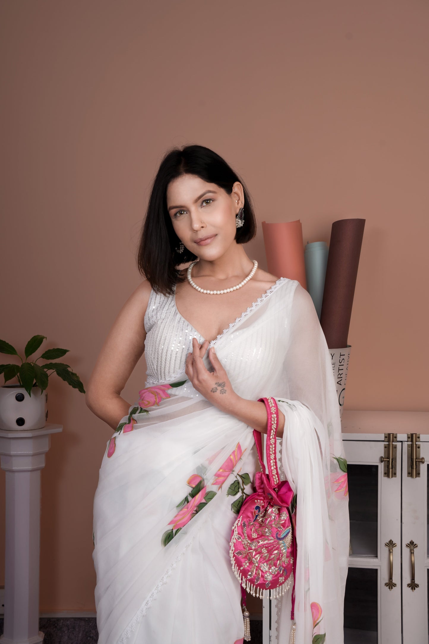 Elegant model wearing a white saree with pink floral print, styled with jewelry and a handbag