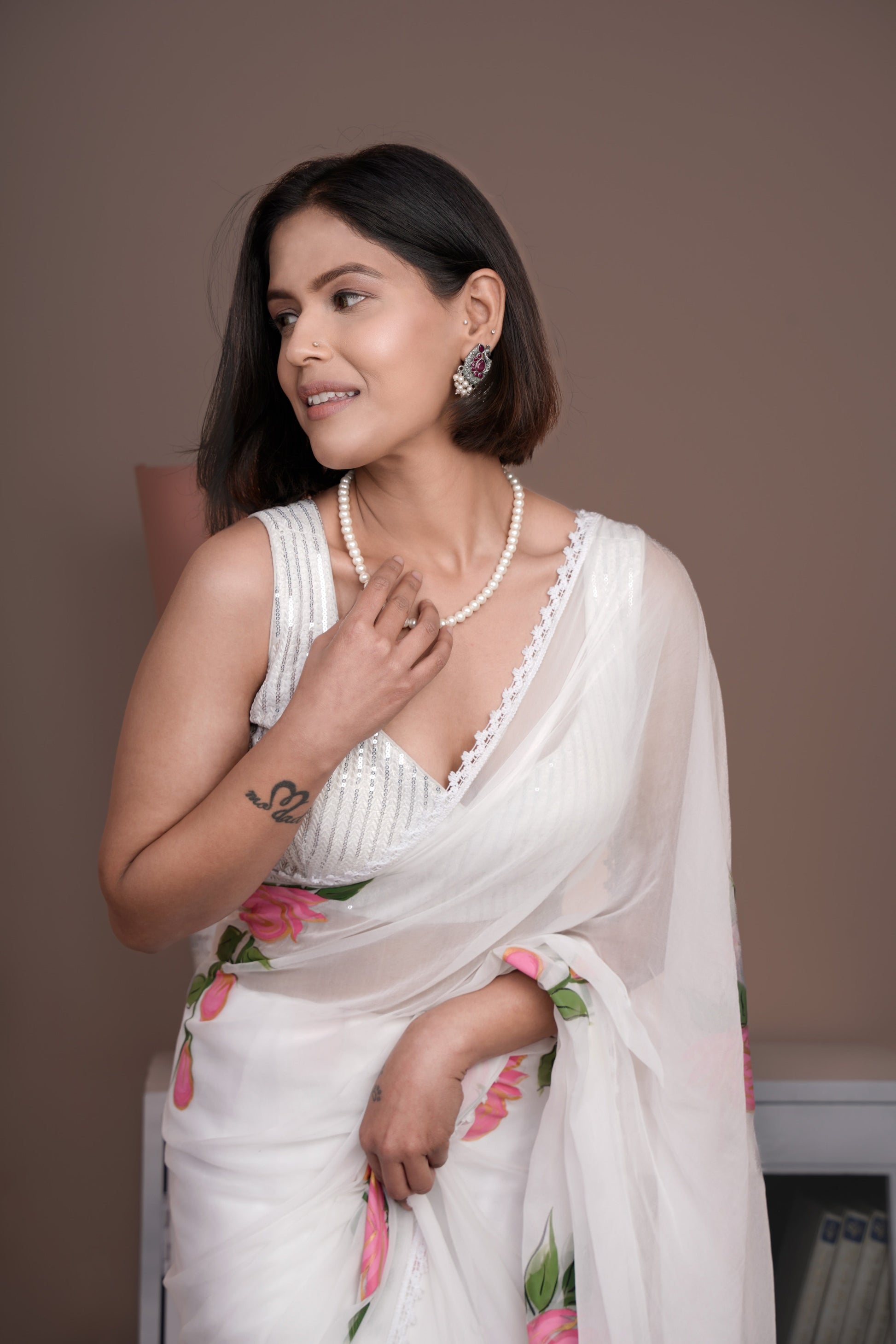 Elegant woman in a white saree with pink floral print, styled with pearls and earrings