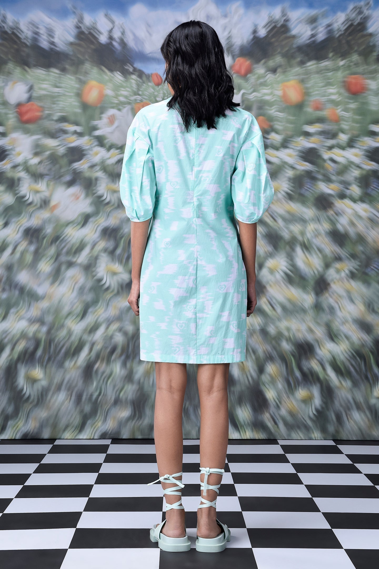 Back view of model wearing mint puff sleeve women's ikkat check casual dress knee length with lace up sandals on check floor