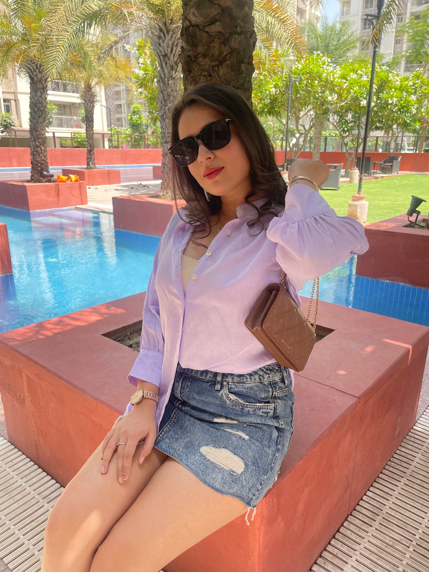 Model wearing a women's lightweight linen shirt in lavender with a stylish denim skirt by a poolside