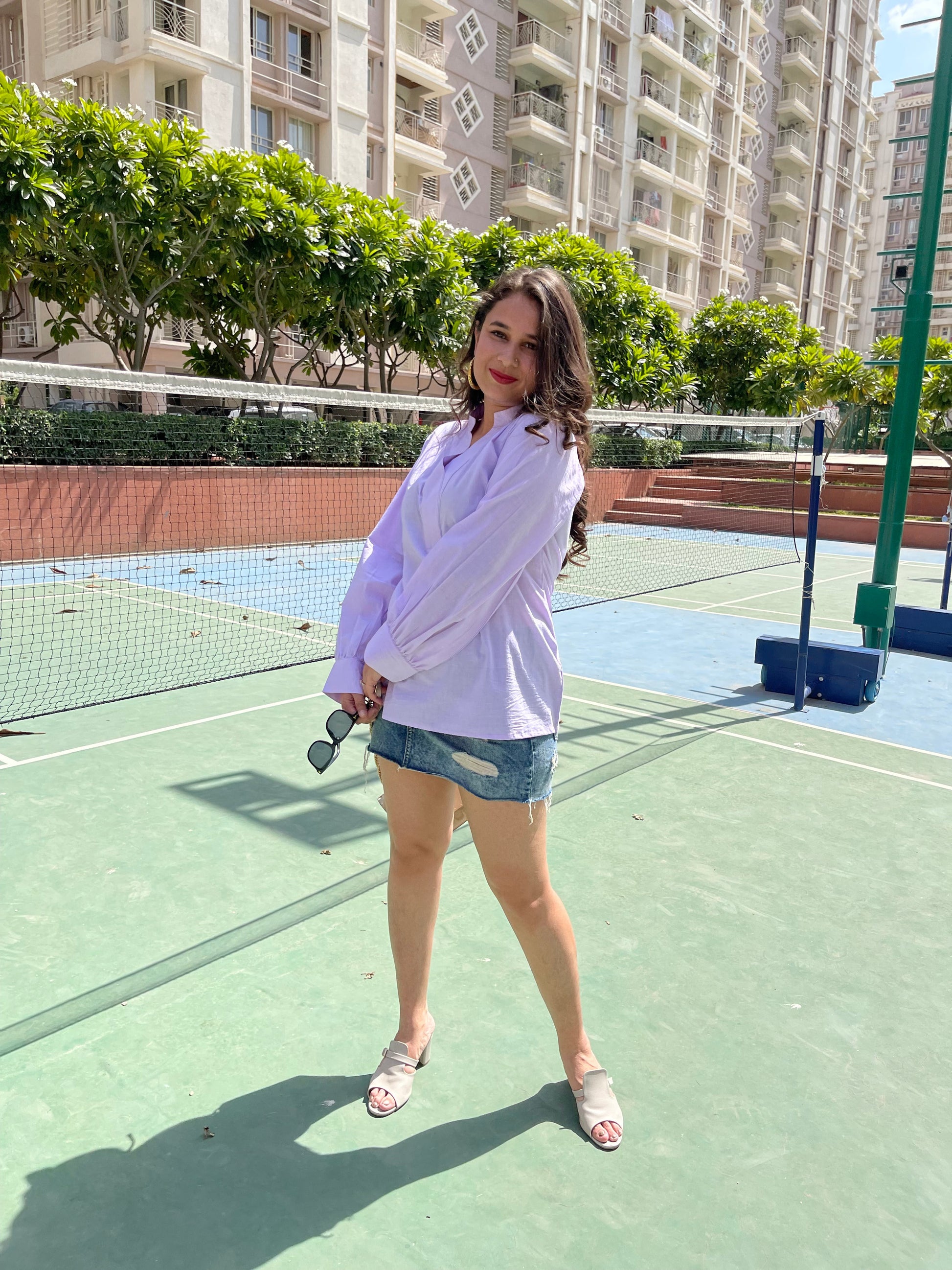 Model wearing a stylish lavender blouse and denim skirt, representing women's trendy summer tops