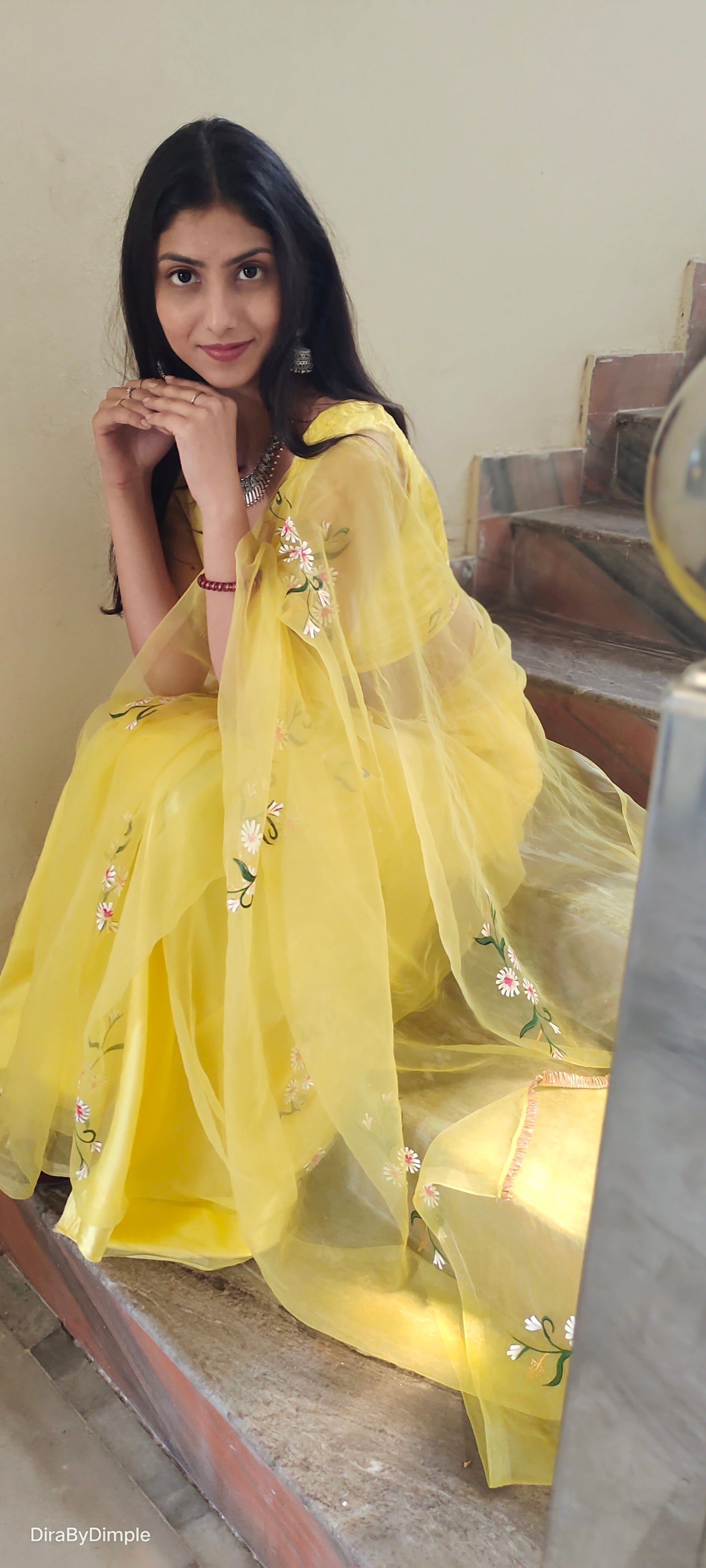 Elegant yellow sunflower saree with floral embroidery, styled gracefully on a model sitting on stairs