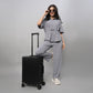 A woman poses confidently in a Grey Tie Up Top with Loose Pants Cord Set and sunglasses, one foot on a black suitcase, against a grey background.
