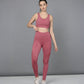 A woman wearing a Peony Pink Netted Top with a honeycomb self pattern and white sneakers stands against a plain gray background.