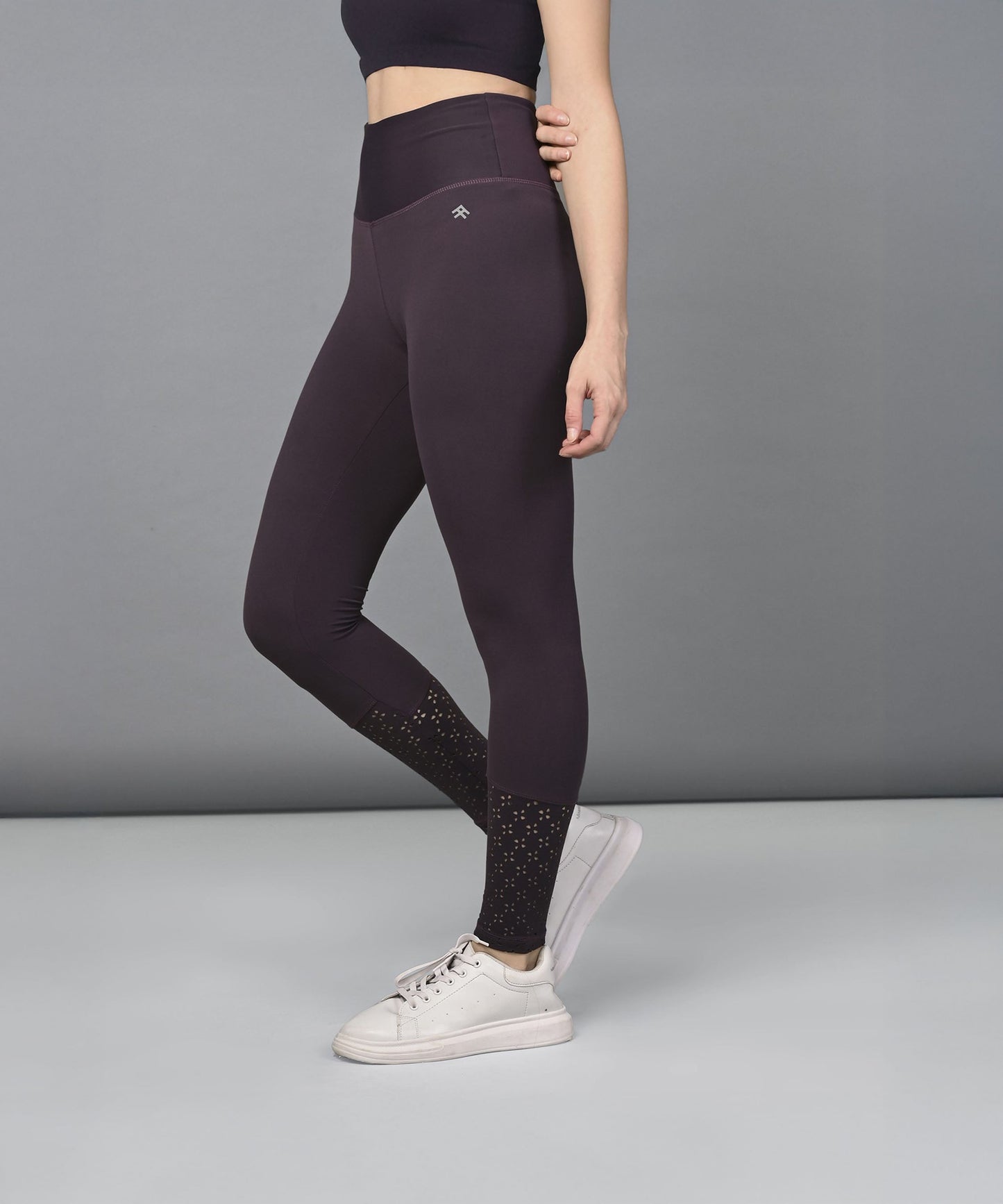 Woman wearing Wine Leggings and white sneakers stands against a plain gray background.