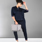 Woman in the Accented Set, a navy cotton co-ord, stands against a plain gray background holding a gray laptop bag.