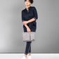 A person wears the Accented Set in navy blue cotton, paired with white shoes and holding a gray bag, standing before a plain gray background.