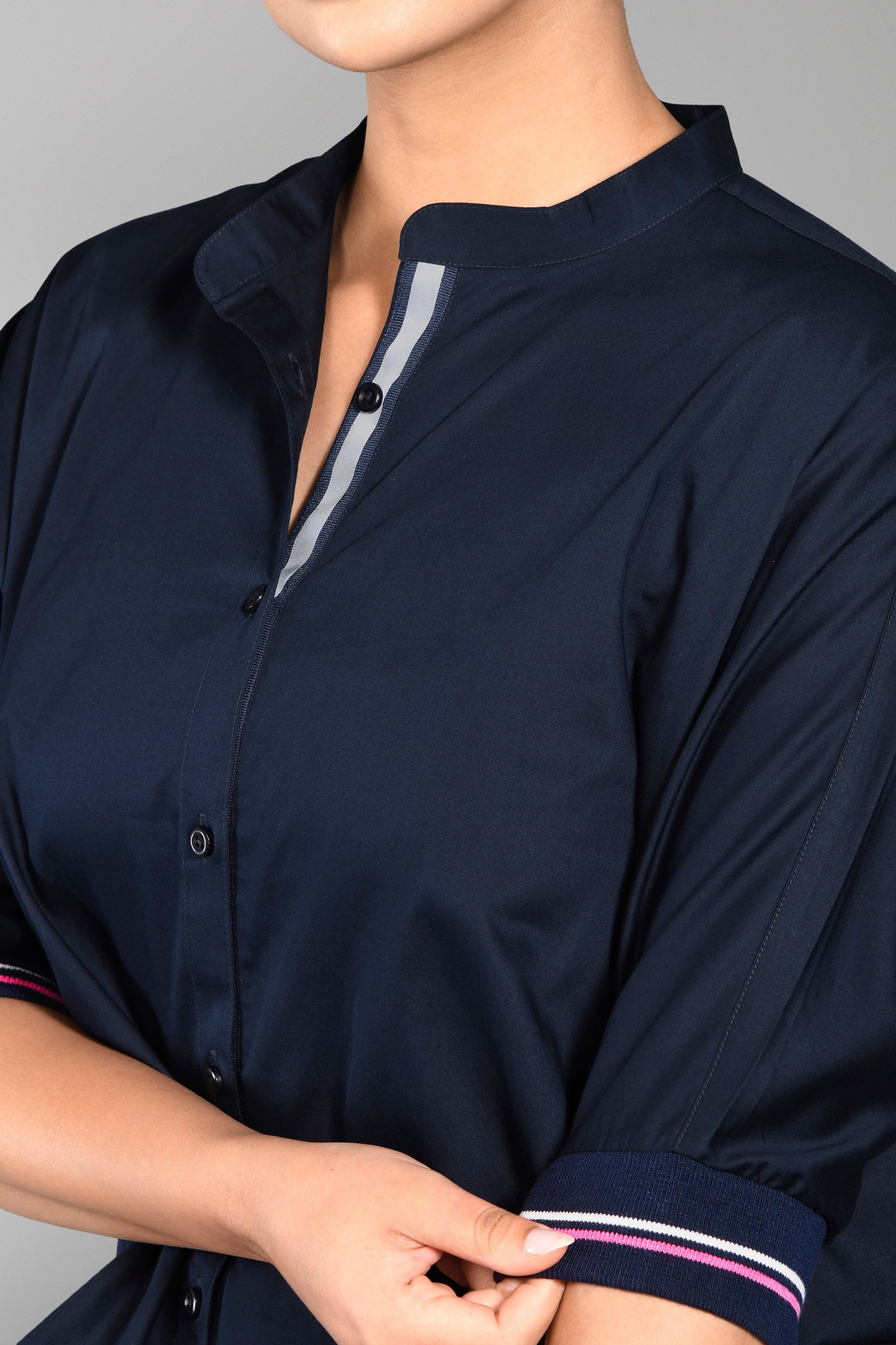Model wears the Accented Set, a navy cotton co-ord featuring distinctive pink-striped sleeves, while adjusting the cuff on their shirt and matching joggers.