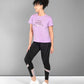 Woman in a Pilates Pink T-shirt, black leggings, and white sneakers standing and smiling.