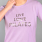 Woman in a Pilates Pink T-shirt with shiny lettering, hand near chin. This stylish and comfortable top enhances your active look.