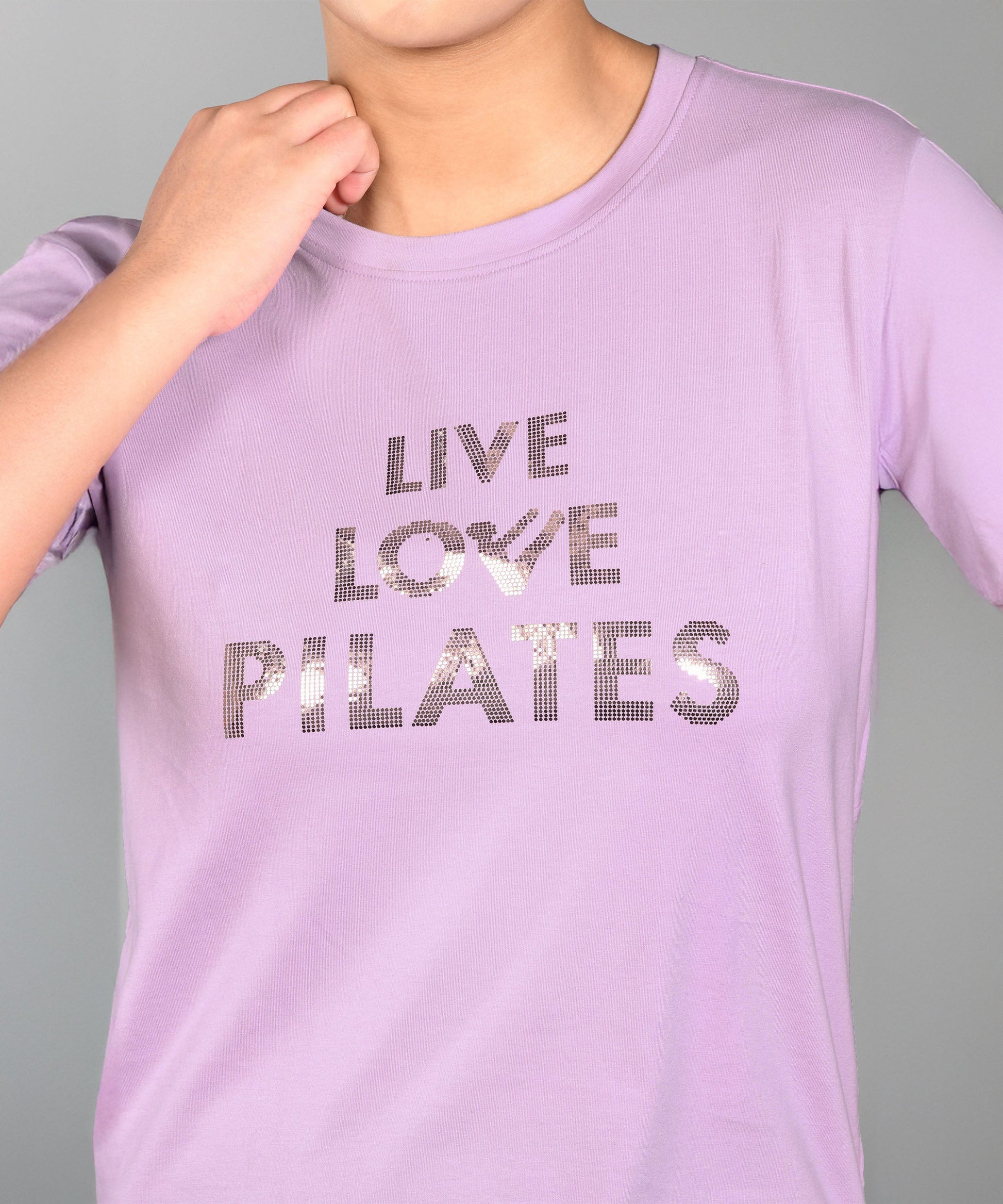 Woman in a Pilates Pink T-shirt with shiny lettering, hand near chin. This stylish and comfortable top enhances your active look.