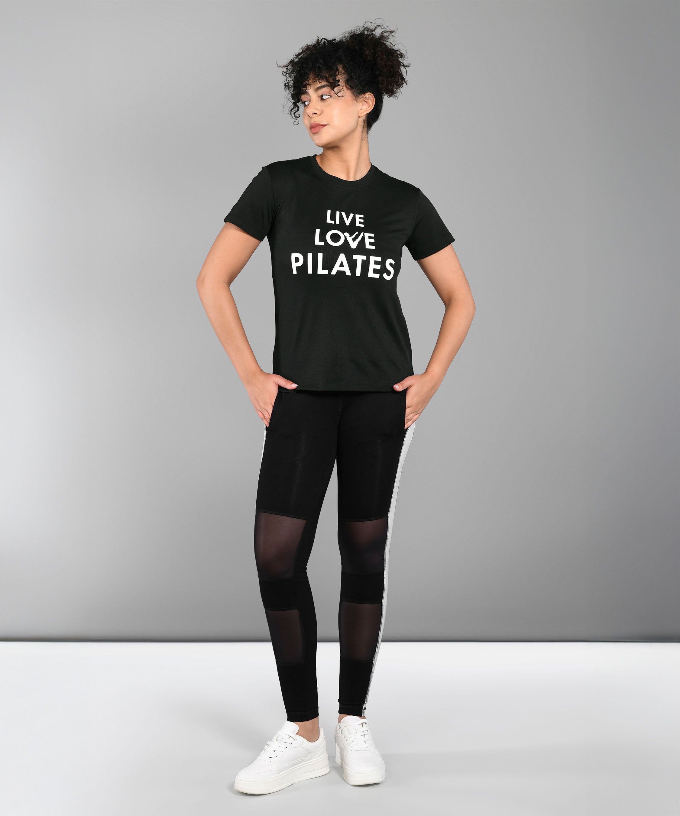 Person wearing a Pilates Black T-shirt and leggings stands with hands on hips against a plain background.