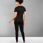 A person stands facing away, wearing a Pilates Black T-shirt, black leggings with white stripes, and white sneakers.