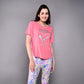 A woman in a pink 'Adore Your Core' Printed Tee smiles and poses in colorful patterned pants against a gray background—the perfect motivational shirt for any workout.