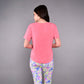 Woman with long dark hair stands with her back to the camera, wearing the pink 'Adore Your Core' Printed Tee and colorful patterned pants.