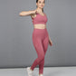 A woman poses confidently against a gray background in the Peony Pink Netted Top paired with white sneakers.