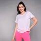 A woman in a light pink 'Pilates Has Your Back' Printed Tee and bright pink leggings smiles confidently against a gray background—the ideal motivational shirt for any Pilates tee collection.