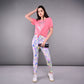 A woman poses against a gray background, holding a camera and wearing the 'Adore Your Core' Printed Tee with colorful leggings—her look radiates energy and confidence.