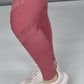 A person wears a Peony Pink Netted Top, pink cut-out leggings, and white sneakers while standing on a light gray surface.