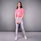 Young woman in the 'Adore Your Core' Printed Tee and patterned leggings holds a tumbler while standing against a plain gray background.