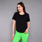 A woman stands against a plain gray background, smiling in the 'Pilates Has Your Back' Printed Tee and bright green pants.