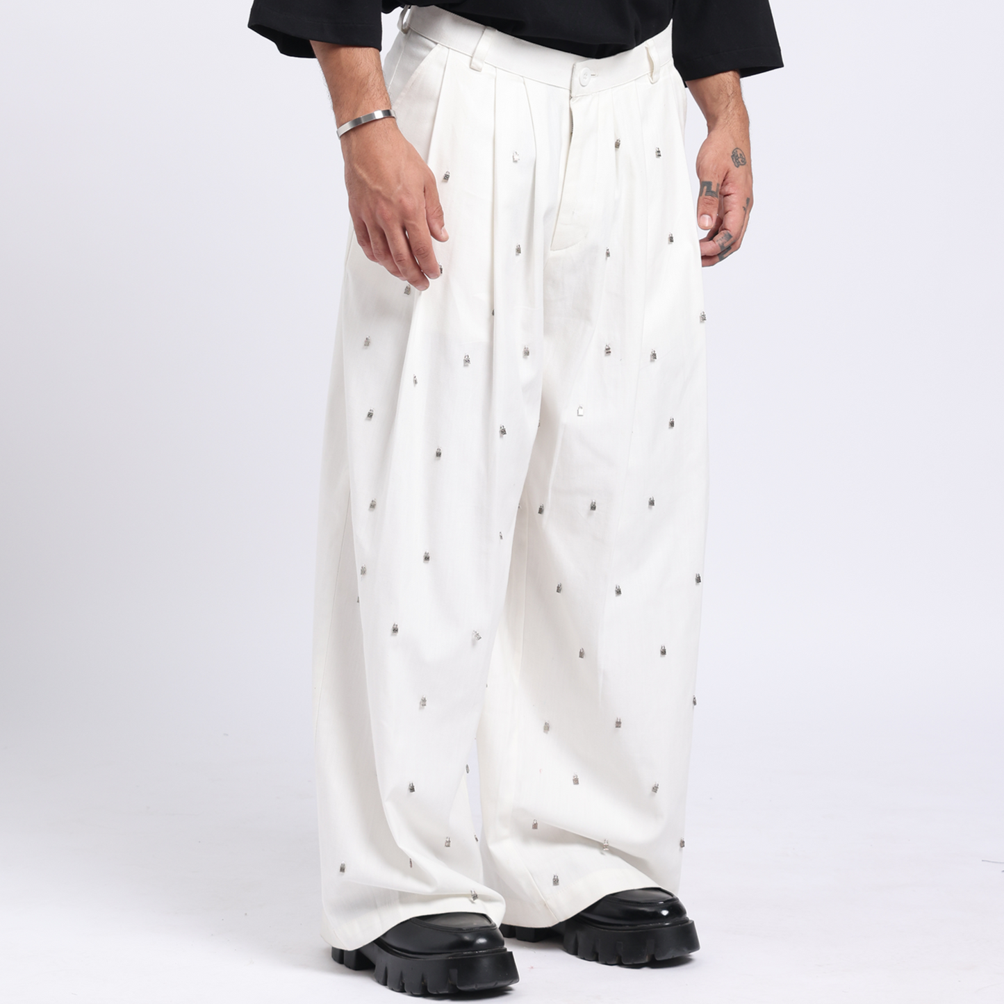 Man wearing a black sweater with a white design and white pants on a white background