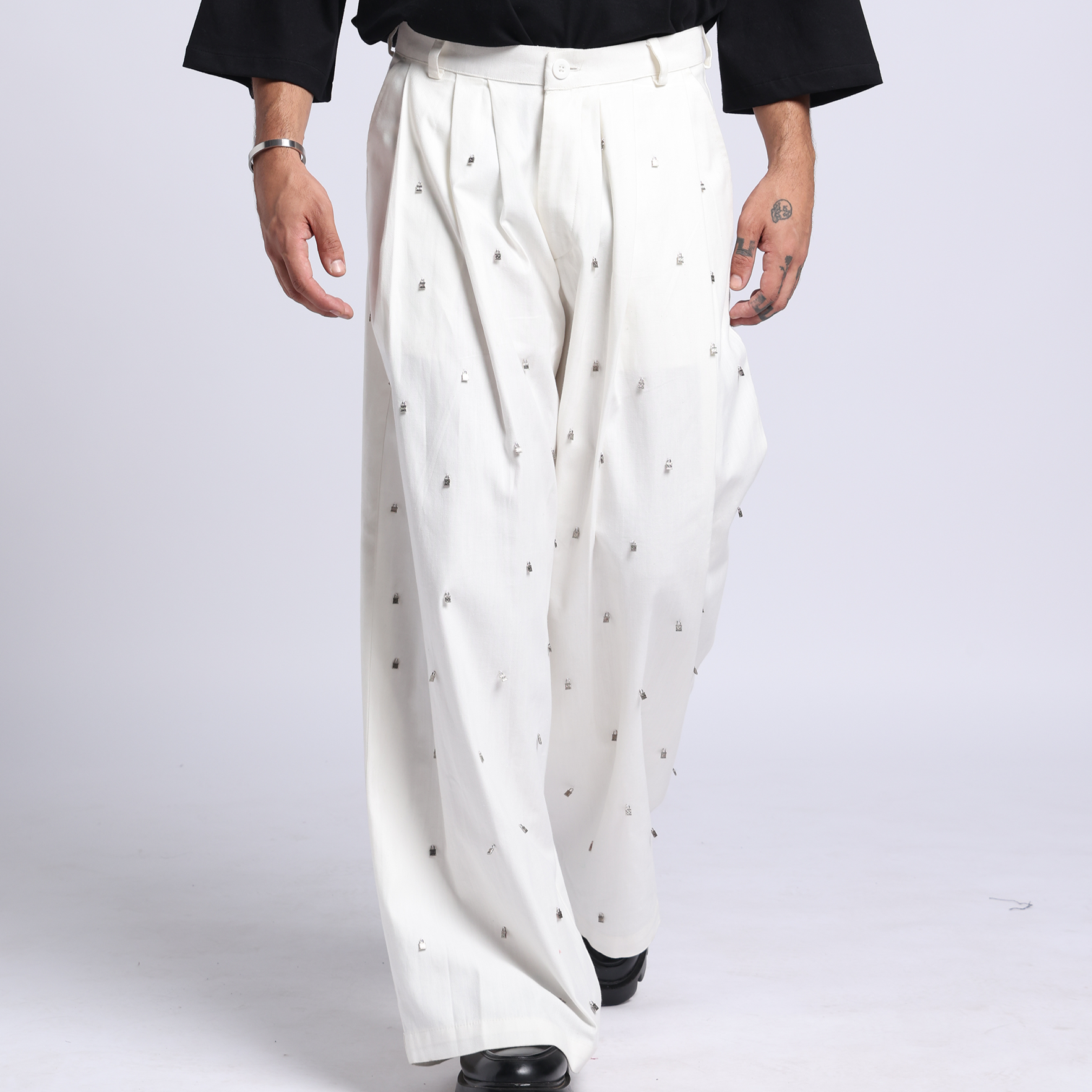 Man wearing a black t-shirt with a white logo and white pants on a white background