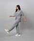A woman wears the Grey Tie Up Top with Loose Pants Cord Set, pairing the coordinated grey outfit with white sneakers as she walks against a plain grey background.