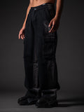A model from the waist down wearing loose-fitting, faded black denim cargo pants with large side pocket flaps. The outfit is paired with chunky black sneakers featuring white graffiti-style lettering on the sides, set against a dark grey studio background.