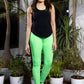 A woman in neon green leggings and a Solid Black Top with Racer Back smiles at the camera while standing on a patio with potted plants.