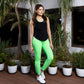 Woman in neon green leggings and a Solid Black Top with Racer Back stands on a wooden deck surrounded by potted plants and palm trees.