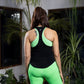 A woman in green leggings and a black tank top stands with her back to the camera, surrounded by plants, showcasing the Solid Black Top with Racer Back, designed for comfort and style.