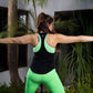 A woman does a yoga pose outdoors among lush plants, wearing the Solid Black Top with Racer Back that keeps her cool and comfortable.