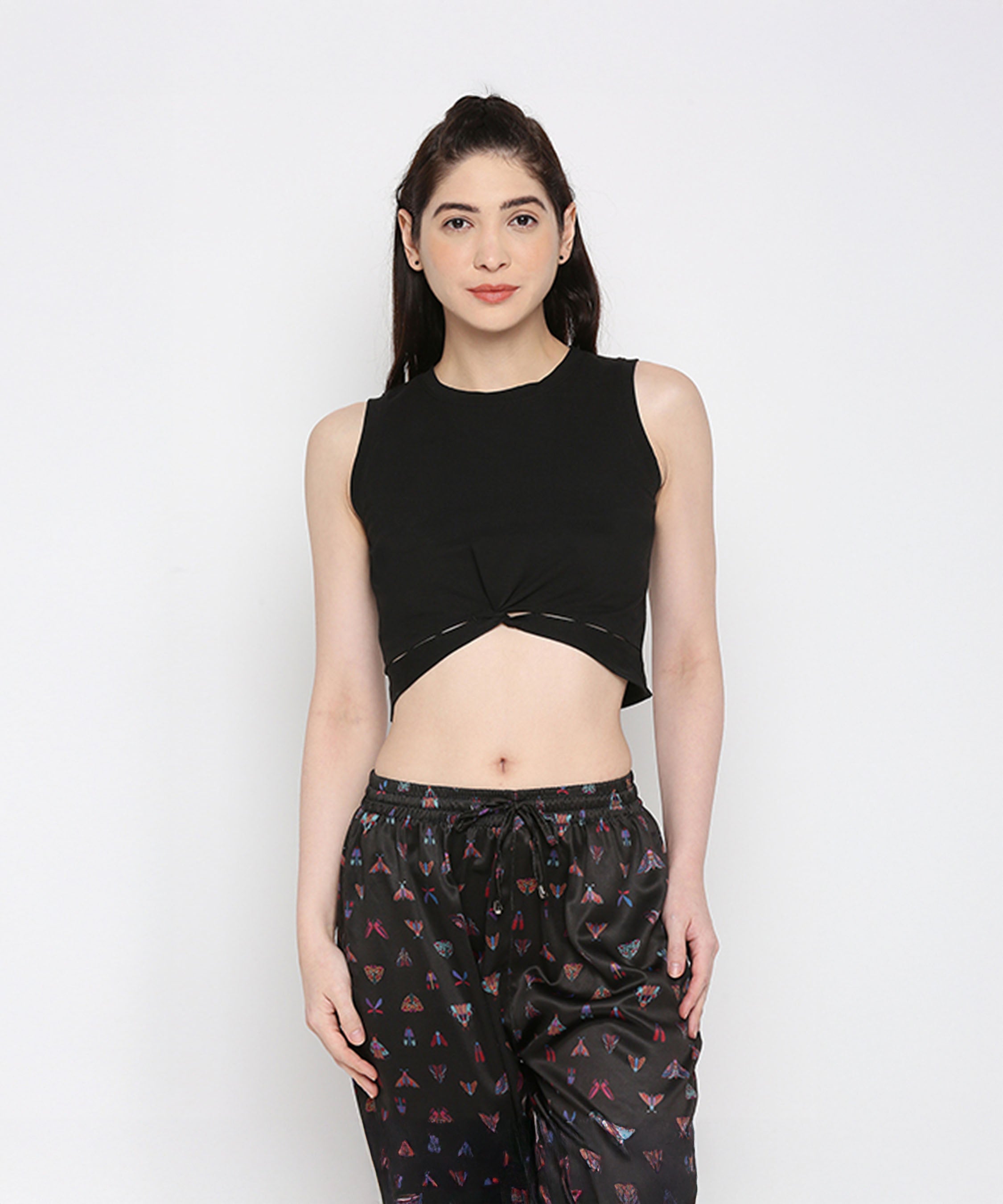 A woman wears the Black Twisted Crop Top with black printed pants, standing against a white background.