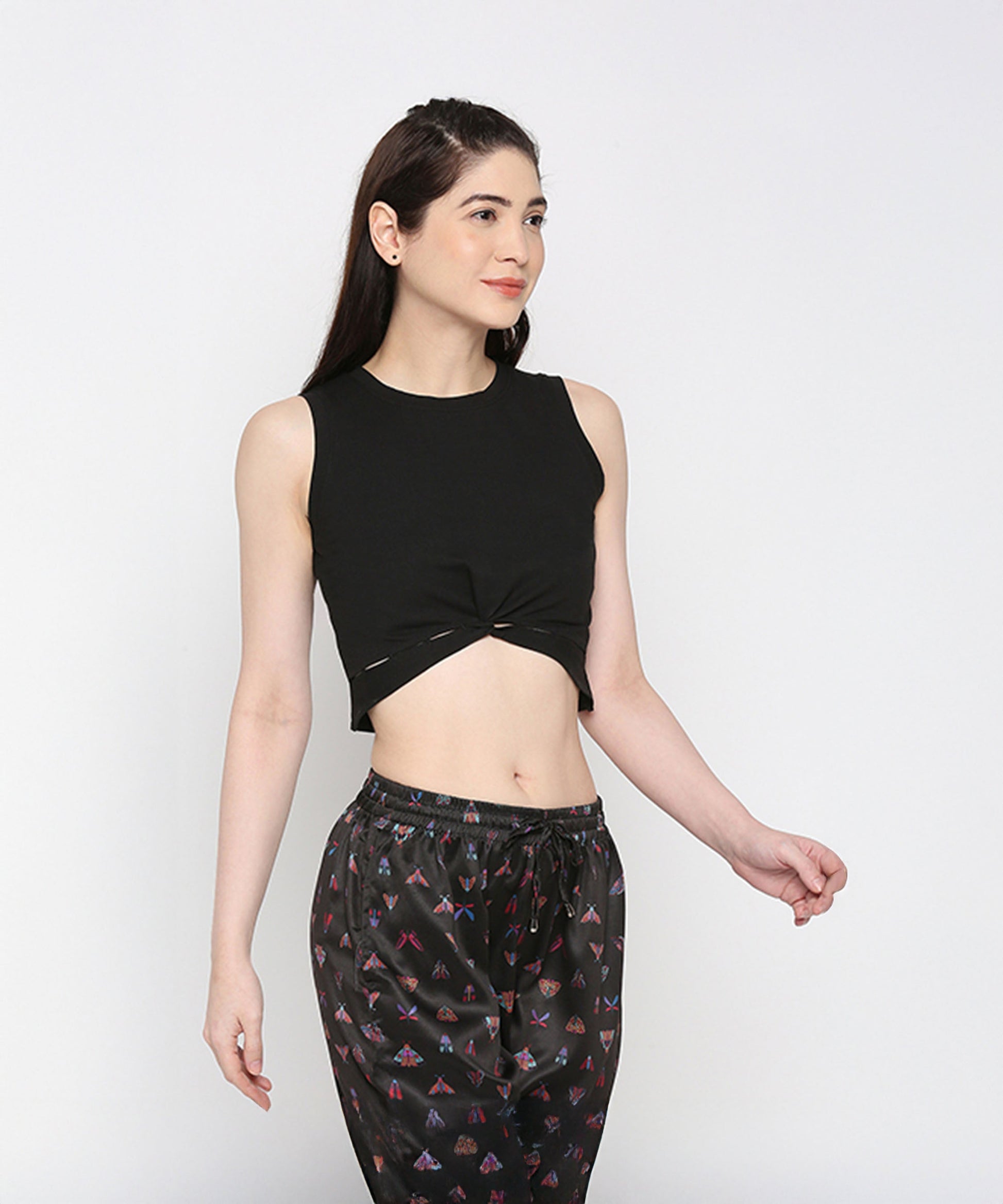 Woman wearing a Black Twisted Crop Top paired with black printed pants, standing against a plain light background.