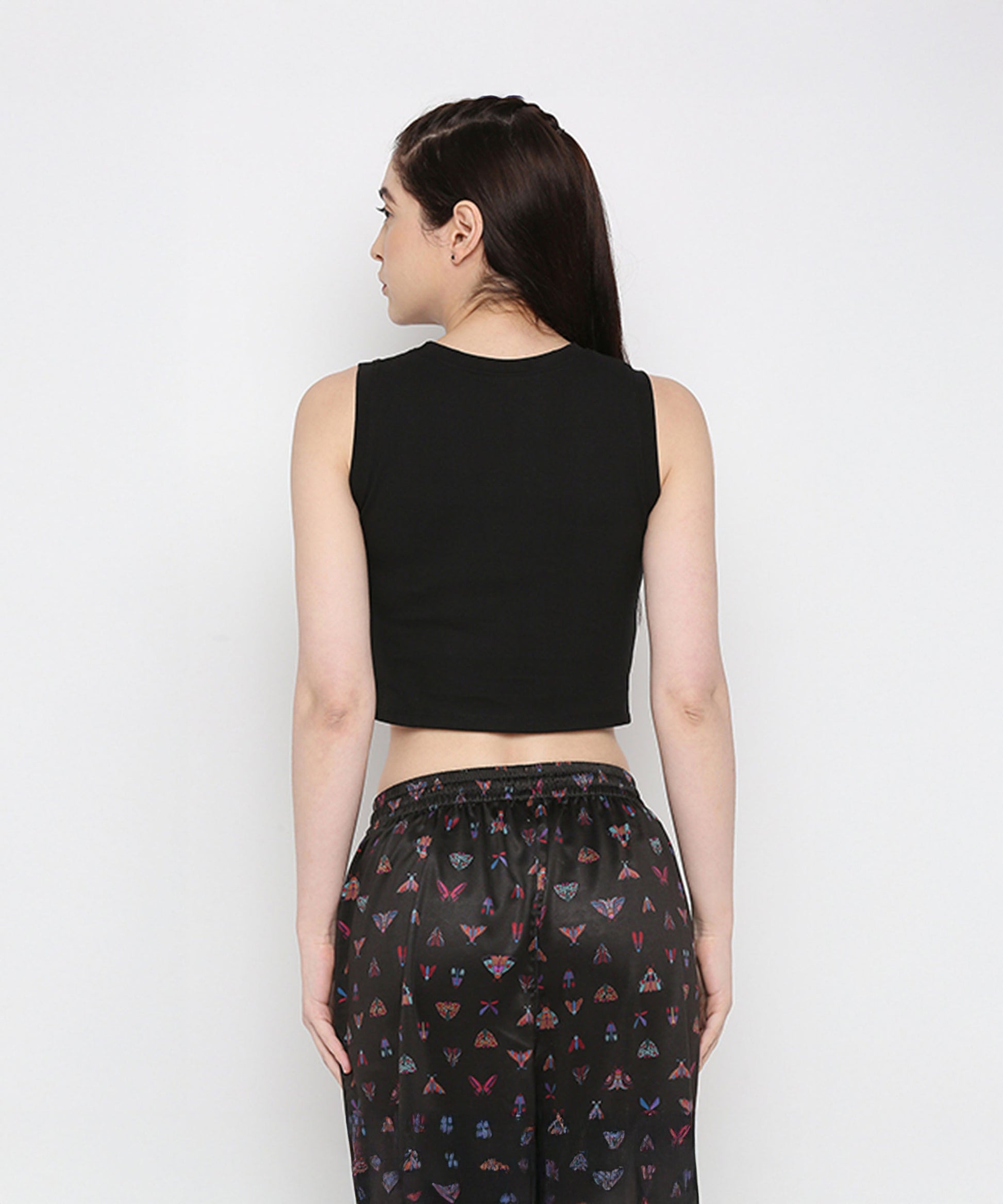 A woman faces away, wearing the Black Twisted Crop Top and printed black pants, set against a plain light background.