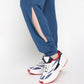 Wearing the Atlantic Blue Active Duo pants, known for their buttery soft fabric and side slit, styled with white sneakers featuring navy and red accents while standing on tiptoe.
