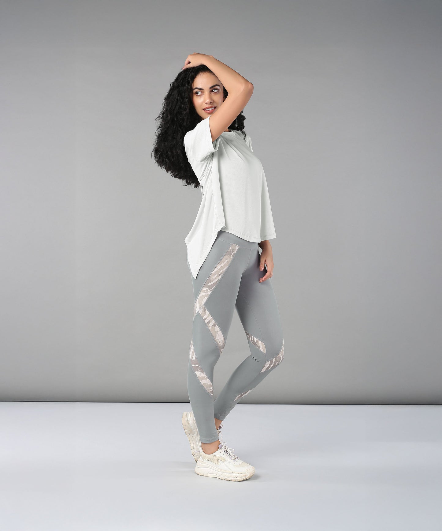 Woman wearing the Grey Top with Patched Legging, made from super soft fabric, poses confidently against a plain grey background.