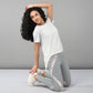 A woman in a Grey Top with Patched Legging kneels and stretches on a plain gray background. The super soft, moisture-wicking fabric of her activewear delivers comfort and keeps her cool throughout her workout.