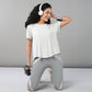 Smiling woman kneeling with headphones and holding a water bottle, dressed in the Grey Top with Patched Legging—workout clothes made from super soft fabric for all-day comfort.